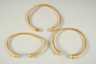 THREE, POSSIBLY INDIAN, HIGH GRADE GOLD BANGLES one with snake finals, the others with balls. Tested