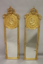 A PAIR OF DECORATIVE GILT FRAMED NARROW MIRRORS, the upper panels depicting female busts. 5ft