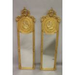 A PAIR OF DECORATIVE GILT FRAMED NARROW MIRRORS, the upper panels depicting female busts. 5ft