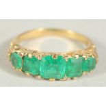 A SIX STONE EMERALD GOLD RING. Size M.