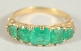 A SIX STONE EMERALD GOLD RING. Size M.