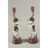 A PAIR OF PORCELAIN SEATED DOG CANDLESTICKS on rectangular bases.