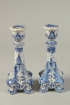 A PAIR OF DUTCH BLUE AND WHITE CANDLESTICKS on four curving legs. 7ins high.