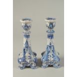 A PAIR OF DUTCH BLUE AND WHITE CANDLESTICKS on four curving legs. 7ins high.