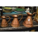 A graduated set of three copper jugs.