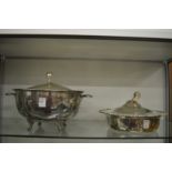 Two large plated serving dishes with lids.