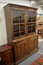 A large oak cupboard bookcase, comprising a pair of glazed doors above a pair of panelled doors.