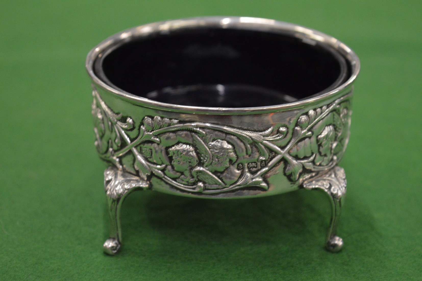 An embossed silver dish with blue glass liner.