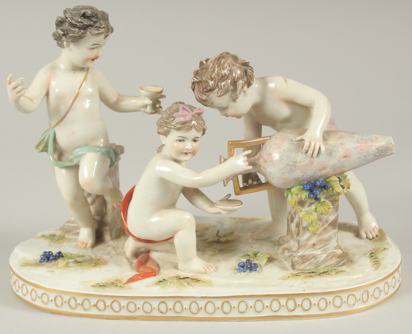 A GOOD PORCELAIN GROUP OF THREE CUPIDS, with a large urn and grapes. 9.5ins long.