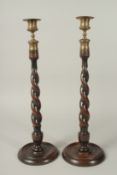A PAIR OF BARLEY TWIST WOODEN CANDLESTICKS with cast metal sconces and circular bases. 20ins high.