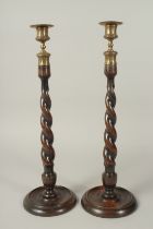 A PAIR OF BARLEY TWIST WOODEN CANDLESTICKS with cast metal sconces and circular bases. 20ins high.