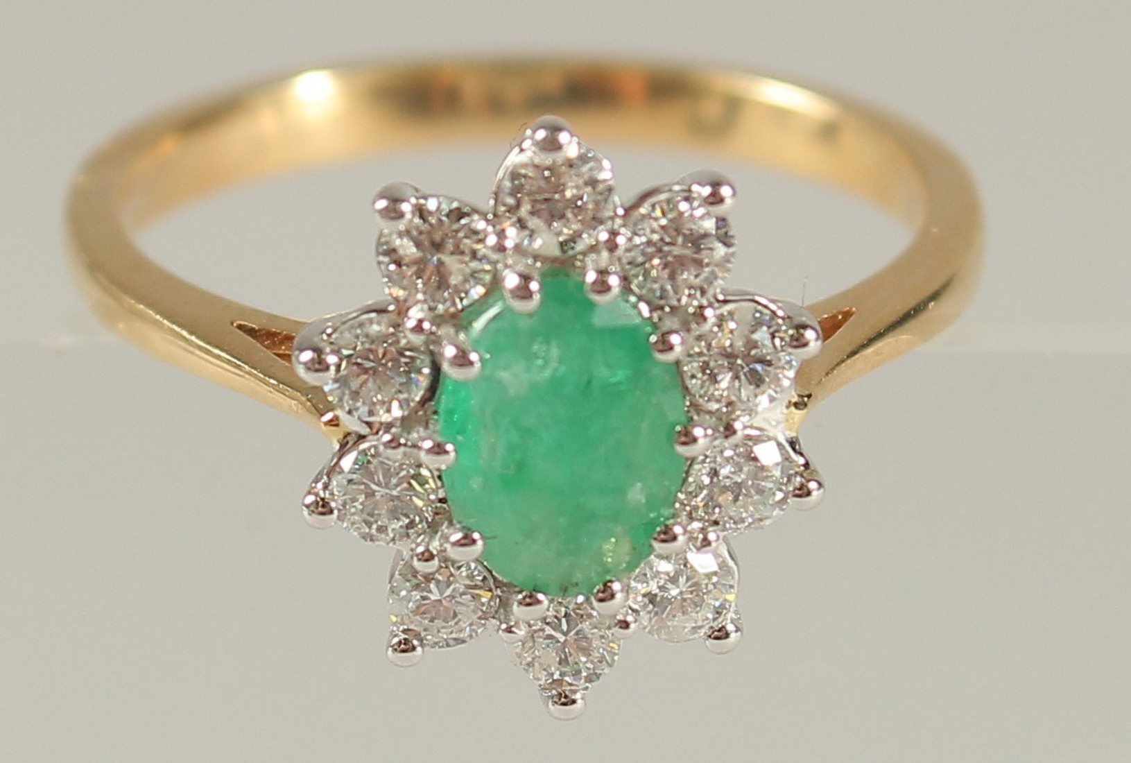 AN 18CT YELLOW AND WHITE GOLD OVAL EMERALD AND RBC DIAMOND CLUSTER RING. Emerald 0.80ct. Diamonds