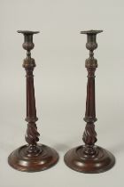 A PAIR OF GEORGIAN STYLE MAHOGANY WOODEN CANDLESTICKS with cast metal sconces, on circular bases.