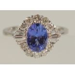 AN 18CT WHITE GOLD OVAL TANZANITE AND DIAMOND CLUSTER RING. Tanzanite 1.34ct. RBC and tapered