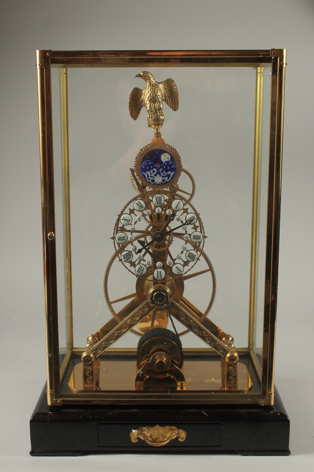 A MOONPHASE BRASS SKELETON CLOCK with eagle, in a glass case. 42cms high.