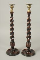 A PAIR OF BARLEY TWIST WOODEN CANDLESTICKS with cast metal sconces and circular bases. 18ins high.