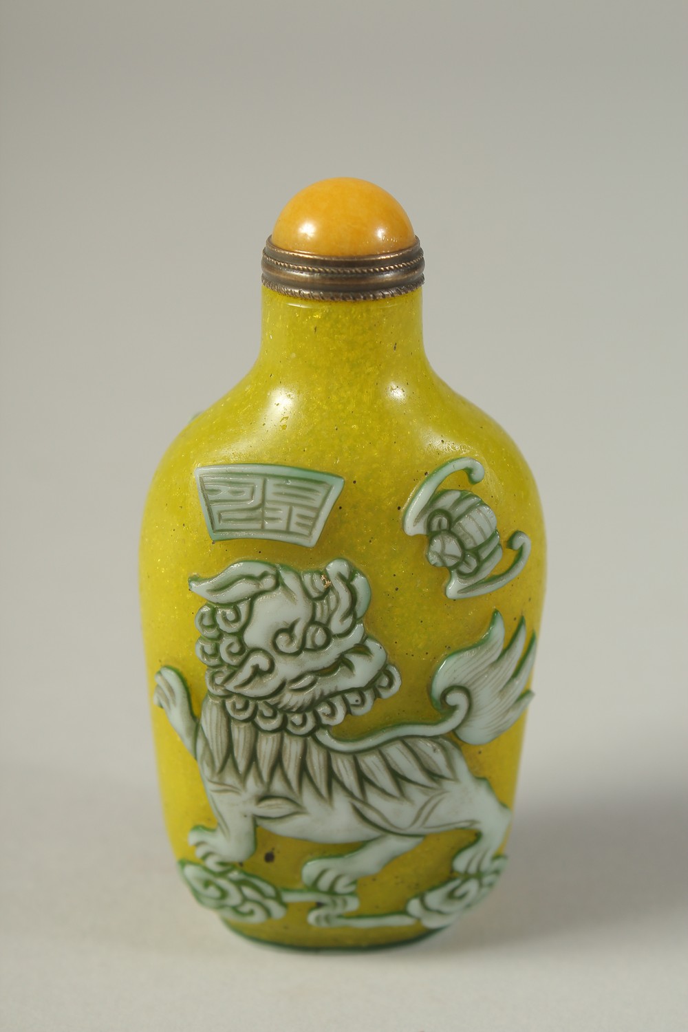 A CHINESE RELIEF-DECORATED FOO DOG SNUFF BOTTLE AND STOPPER / SPOON, 8cm high.