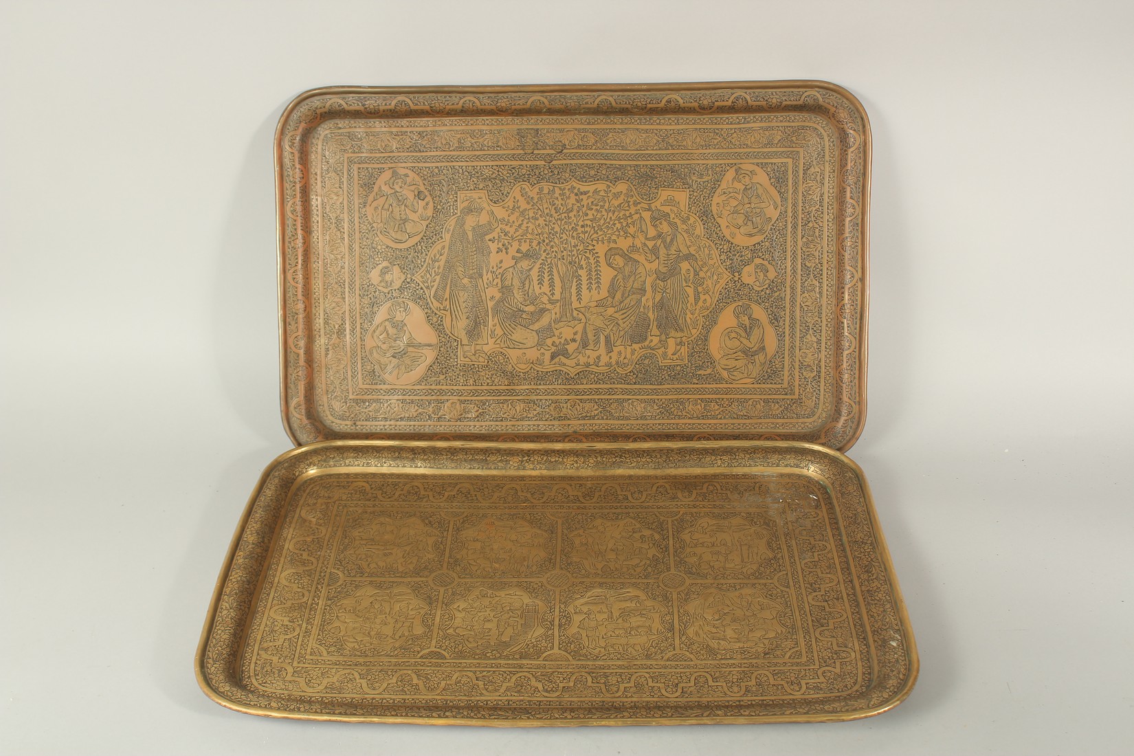 TWO FINE PERSIAN QAJAR BRASS ENGRAVED TRAYS, with pictorial panels, 58cm x 37.5cm and 58.5cm x 38.