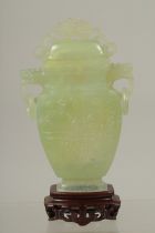 A CHINESE CARVED JADE LIDDED VASE AND WOODEN STAND, the vase with archaic style carving and drop