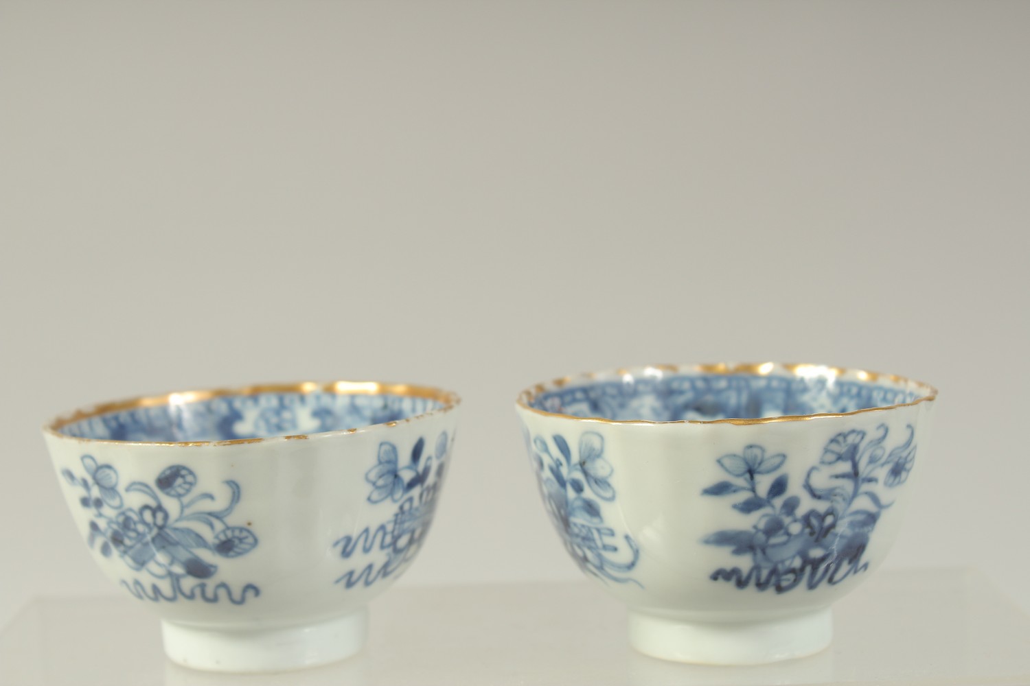 A PAIR OF CHINESE BLUE AND WHITE PORCELAIN TEA BOWLS, with gilded rims and decorated with precious