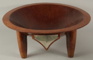A VERY LARGE FIJIAN KAVA CARVED HARDWOOD BOWL, raised on four legs, with mounted metal plaque