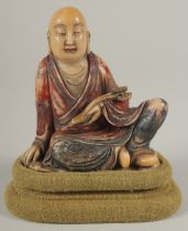 A CHINESE CARVED HARDSTONE FIGURE OF LUOHAN, holding ruyi scepter, with fabric overlaid stand and