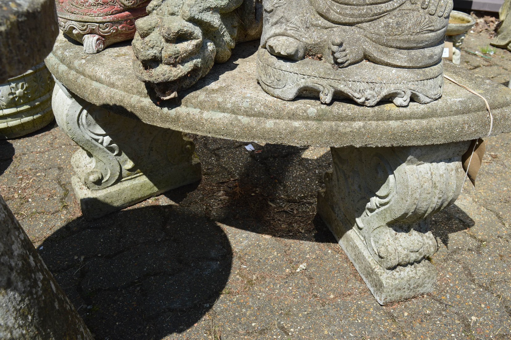 A reconstituted stone semi-circular garden bench seat with scrolling supports.