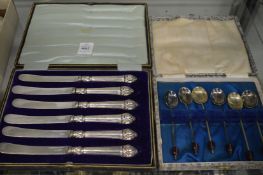 A cased set of six silver handled tea knives and a cased set of six plated coffee bean spoons.