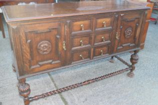 A 1930s quarter cut oak sideboard, fitted three drawers and flanking cupboards, on turned and