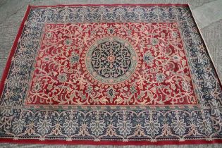 A machine-made woollen carpet of traditional Persian design with foliate motifs, on a crimson ground