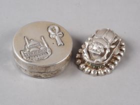 An Egyptian silver oval pill box with scarab beetle lid and an Egyptian silver circular pill box and