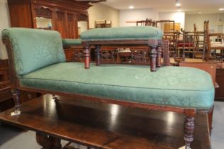 An early 20th century carved mahogany chaise longue, upholstered in a green figured fabric, on