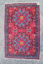 A Kazak rug with two blue and red star medallions, on a red ground with animals and flowers, 30" x