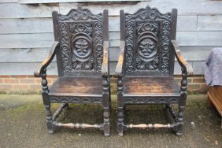 A pair of carved oak elbow chairs of early 17th century design with lion mask panel back, on