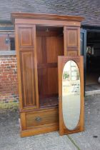 An Edwardian walnut and satinwood banded wardrobe enclosed oval mirror panel door over one long