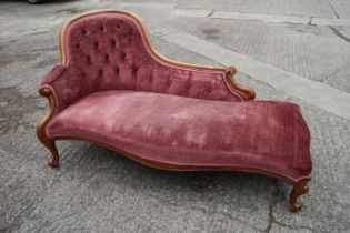 A late Victorian carved walnut showframe chaise longue, upholstered in a claret velour, on