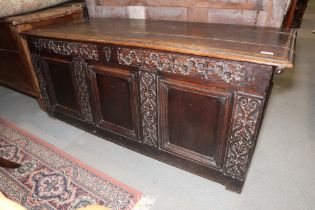 An early 18th century carved oak triple panel front coffer with scroll design and planked top, on
