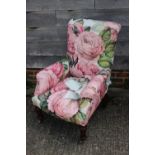 An early 20th century walnut framed low seat armchair, upholstered in a floral fabric, on turned and