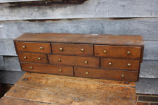 An oak table top nest of eight drawers with brass knob handles, 33 1/4" wide x 7" deep x 9 3/4" high