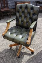 A walnut framed desk chair with back button upholstered in a green leather, on splayed and