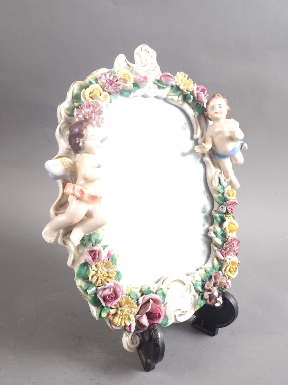 A Continental porcelain framed wall mirror with relief decoration of cherubs and flowers, 10" high