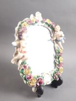 A Continental porcelain framed wall mirror with relief decoration of cherubs and flowers, 10" high