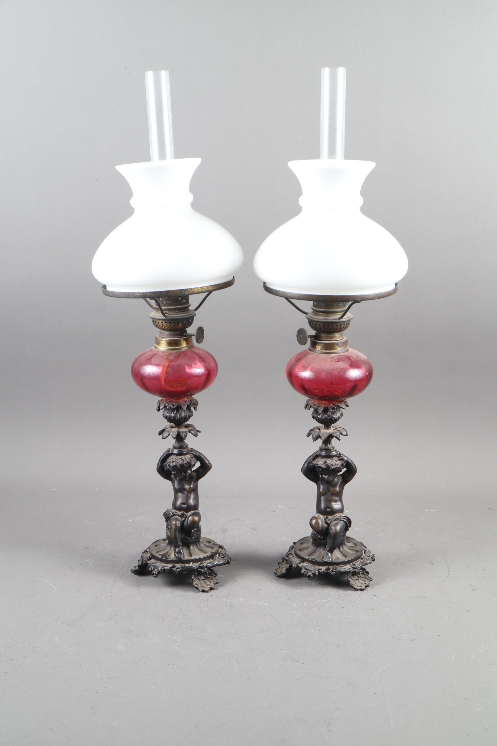 A pair of early 19th century patinated candlesticks, formed as putti, with later added ruby glass