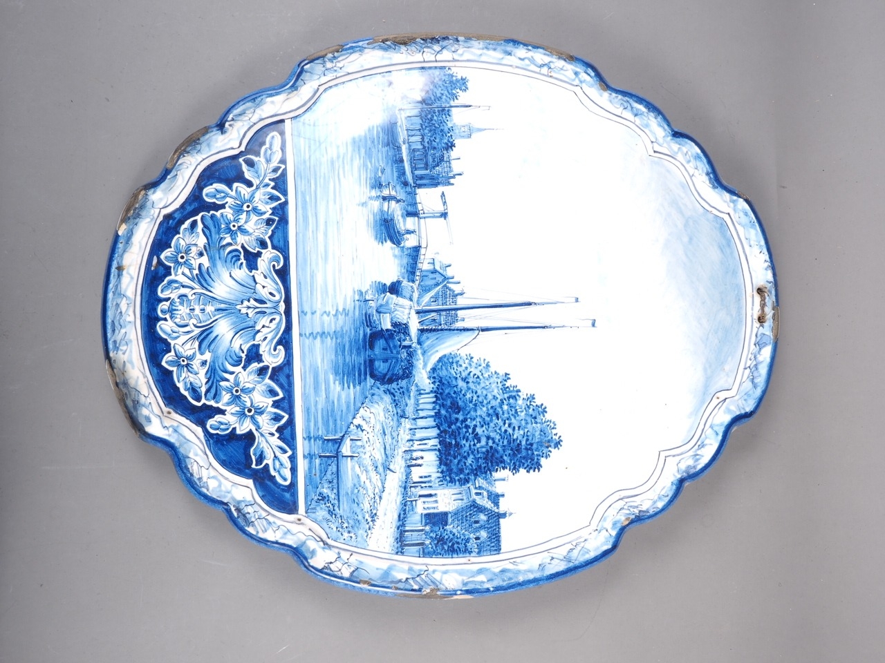 A Delft blue and white shaped wall plaque with boats in a river decoration, 19 3/4" high x 16 1/2"