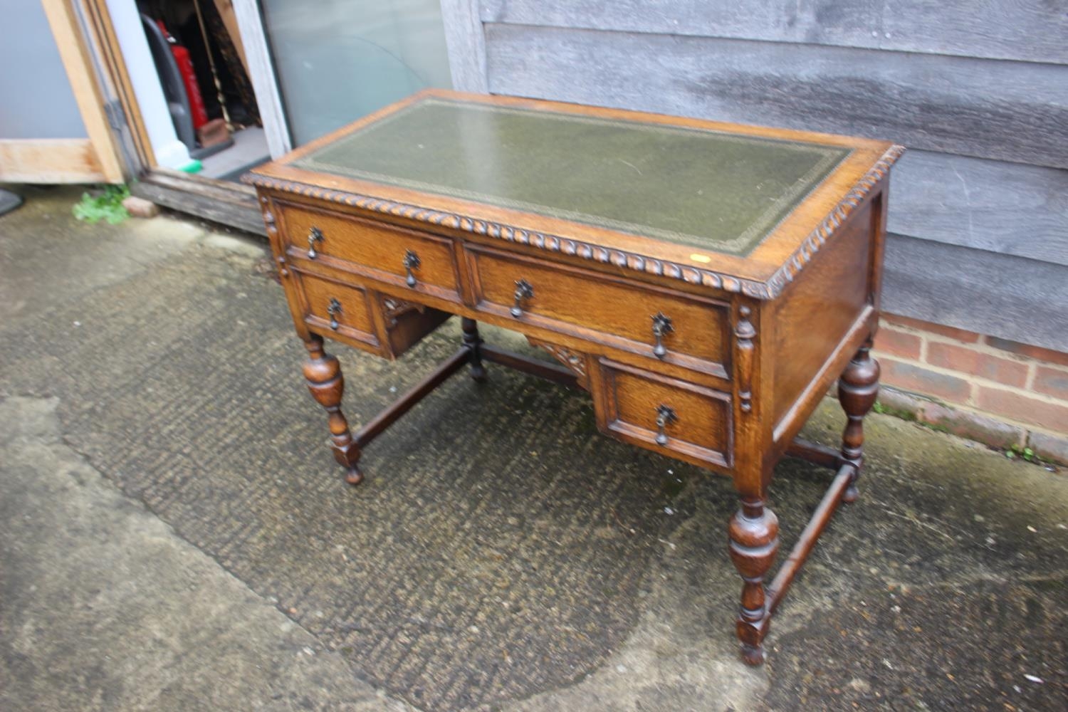 A carved oak desk with green leather lined top over four drawers, on turned and stretchered