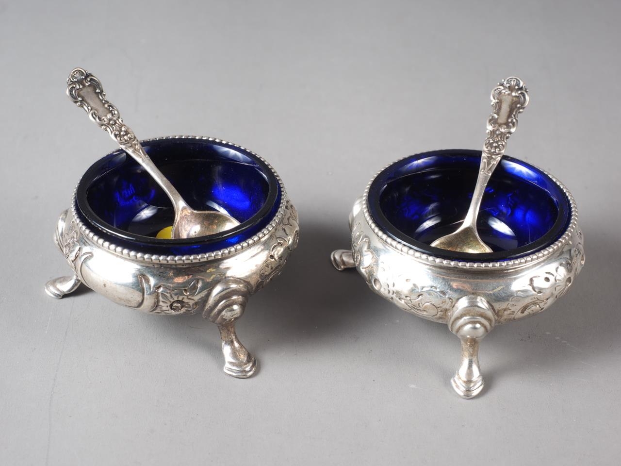A pair of Victorian silver cauldron salts with embossed decoration, blue glass liners and a pair