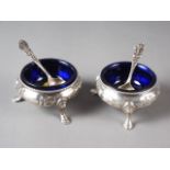 A pair of Victorian silver cauldron salts with embossed decoration, blue glass liners and a pair