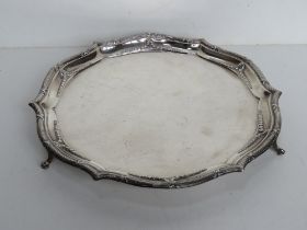 A hallmarked silver salver raised over three outswept feet,