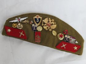 A Russian side cap with various military badges upon.