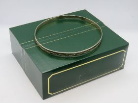 A 9ct gold bangle having etched design, 5.2g, 6.5 x 7cm dia, in presentation box.